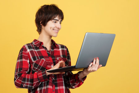 Androgynous person smiling while using a laptopの写真素材