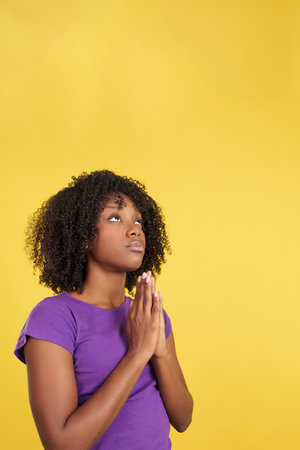 Afro woman praying while looking up joining handsの写真素材