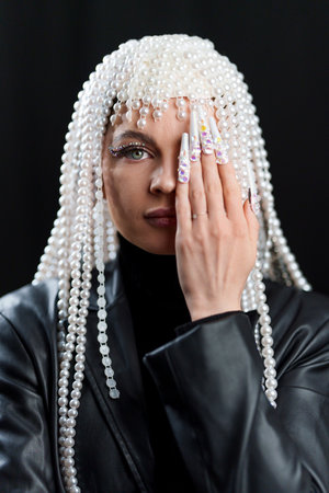 Woman with wig of pearls covering one eye with handの写真素材