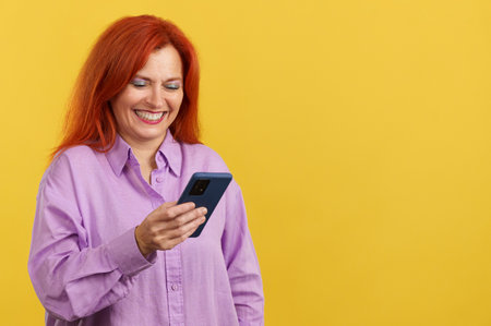 Happy mature redheaded woman smiling while using the mobileの写真素材