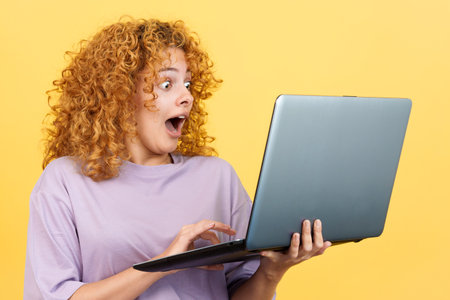 Surprised woman with curly hair using a laptop standingの写真素材