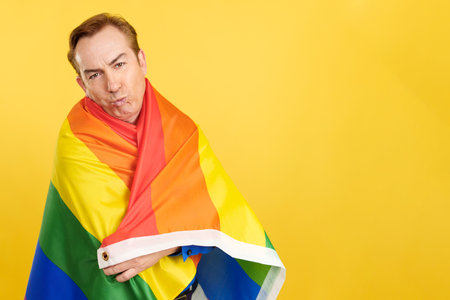 Mature man kissing while wrapping with a lgbt flagの写真素材