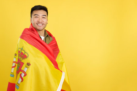 Happy chinese man wrapping with a spanish national flagの写真素材