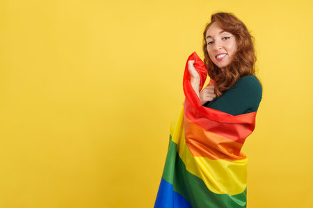 Happy redheaded woman wrapped with a lgbt flagの写真素材