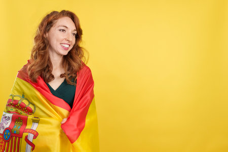 Happy redheaded woman wrapping with a spanish national flagの写真素材