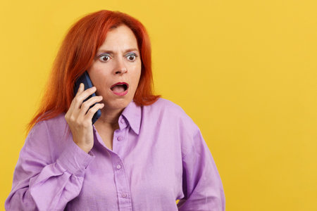 Surprised mature redheaded woman talking to the mobileの写真素材