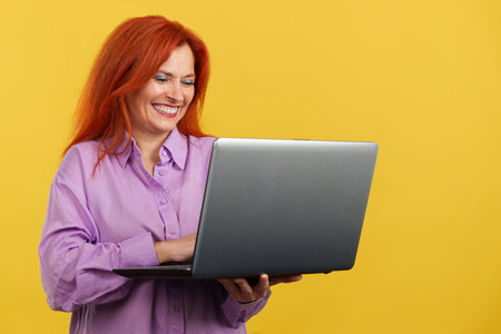 Redheaded mature woman smiling while using a laptopの写真素材