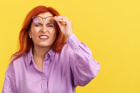 Aged redheaded woman taking off her glasses to seeの写真素材
