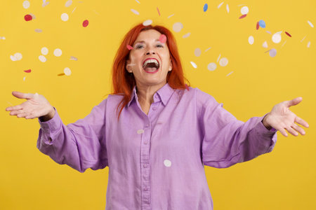 Redheaded mature woman surrounded by confetti flying in the air
