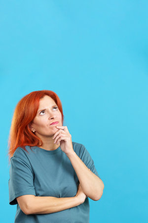 Redheaded mature woman with hand on face and thoughtful expressionの写真素材