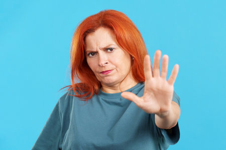 Redheaded mature woman gesturing prohibition with handの写真素材