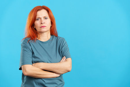 Serious mature redheaded woman looking at camera with arms crossedの写真素材