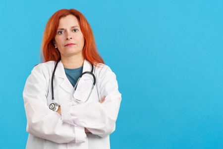 Serious mature redheaded female doctor standing with arms crossedの写真素材