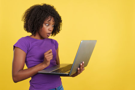 Woman with afro hair looking a laptop with shocked expressionの写真素材