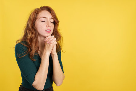 Redheaded woman praying with folded hands and eyes closedの写真素材