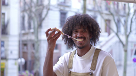 Man with afro hairstyle eating pizza pulling on melted cheeseの写真素材
