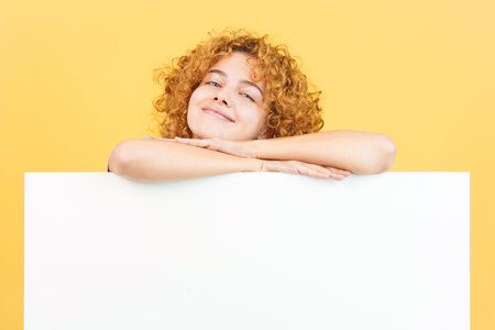 Relaxed woman with curly hair leaning on a blank panelの写真素材