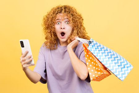 Surprised woman using the mobile while holing shopping bagsの写真素材