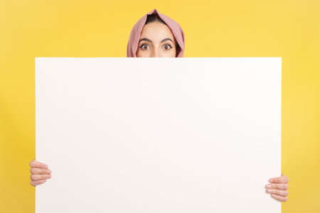 Surprised muslim woman hiding behind a blank panelの写真素材