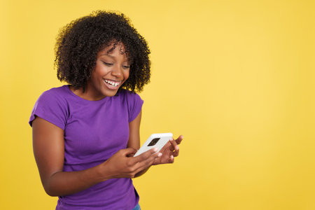 Happy woman with afro hair smiling while reading a mobileの写真素材