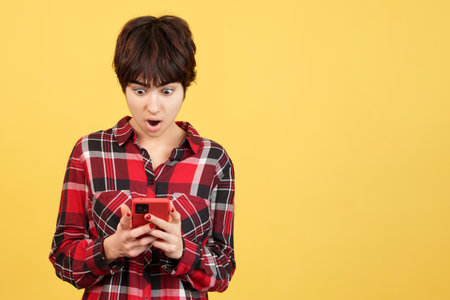 Androgynous person looking at the mobile with surprised expressionの写真素材