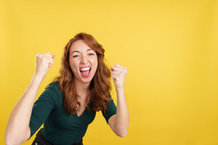 Happy redheaded woman celebrating raising the fistsの写真素材