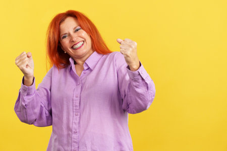 Happy mature woman celebrating while raising armsの写真素材