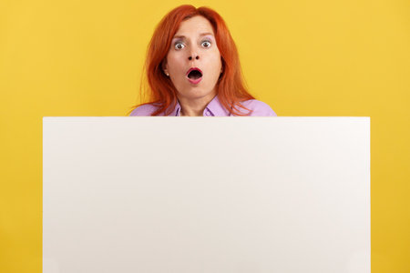 Amazed redheaded mature woman hair holding a blank panelの写真素材