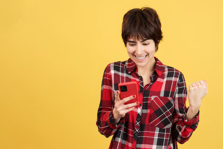Androgynous person celebrating while using a mobileの写真素材