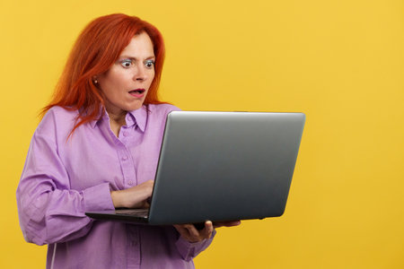 Redheaded mature woman with a surprised look using a laptopの写真素材