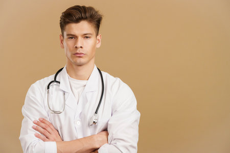 Handsome serious doctor looking at camera standing with arms crossedの写真素材