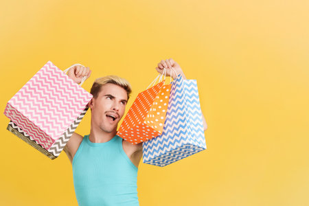 Cute gay man raising many shopping bags while smilingの写真素材