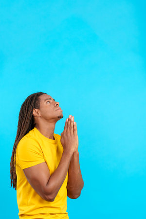 Latin man with dreadlocks looking up praying with folded handsの写真素材