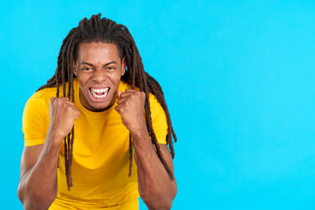 Happy hispanic man with dreadlocks gesturing with fists while celebratingの写真素材