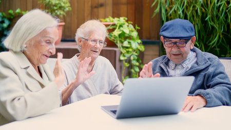Seniors using laptop and waving during a video call outdoorsの写真素材