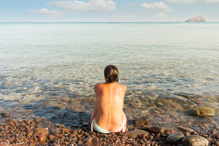 Woman sitting on the seashore with her back turnedの写真素材