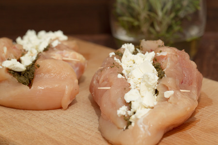 Raw chicken breasts with pesto and feta on wooden cutting boardの写真素材