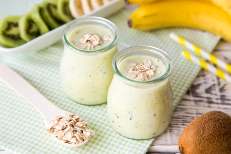 Banana smoothie with kiwi and oats on a light wooden table. Protein diet. Healthy food concept.の写真素材