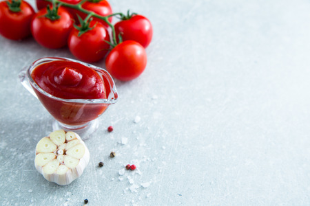 Tomato ketchup sauce with garlic, spices and herbs with cherry tomatoes in a glass bowl on stone table, selective focus. Copy spaceの写真素材