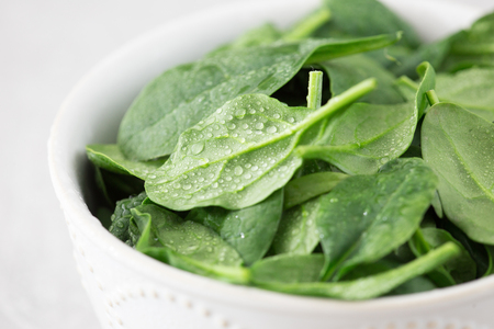 Washed fresh mini spinach in a plate on an stone background.の写真素材