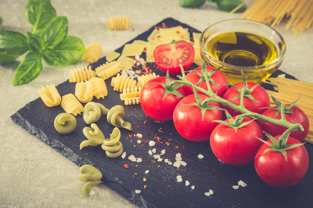 Pasta ingredients. Cherry tomatoes, pasta, fresh basil, spices on a  stone background, closeup, selective focus.の写真素材