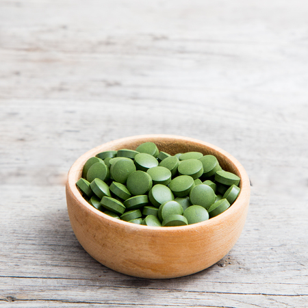 green pills spirulina or chlorella seaweed in the wooden bowl. green barley chlorella.の写真素材