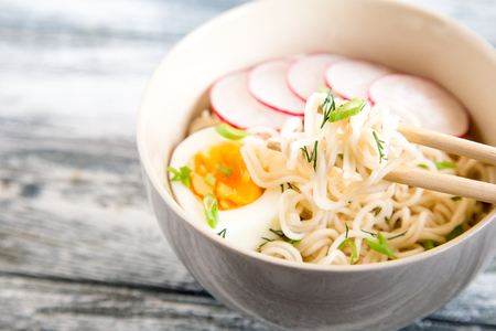 Instant noodles on wooden background. Cooked chinese instant noodles. Soup Ramen with egg and radishの写真素材