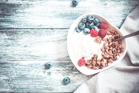 Greek yogurt, blueberries, raspberries and granola in a white bowl on a wooden background.の写真素材
