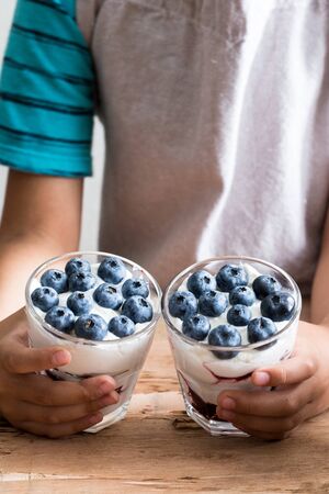 boy holds homemade dessert with greek yogurt or cream, blueberry jam and fresh blueberries.の写真素材