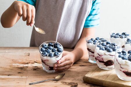 boy holds homemade dessert with greek yogurt or cream, blueberry jam and fresh blueberries.の写真素材