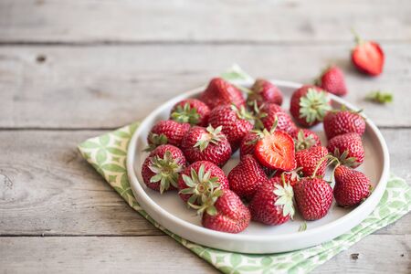 ripe juicy strawberries in a clay plate on a light background with copy spacの写真素材