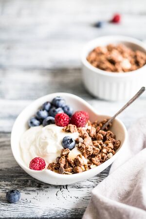 Greek yogurt, blueberries, raspberries and granola in a white bowl on a wooden background.の写真素材