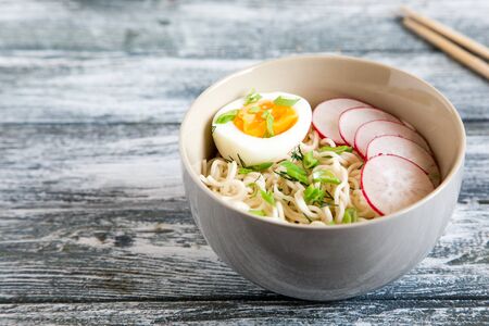 Instant noodles on wooden background. Cooked chinese instant noodles. Soup Ramen with egg and radishの写真素材