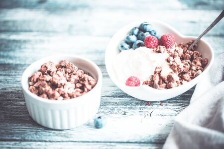 Greek yogurt, blueberries, raspberries and granola in a white bowl on a wooden background.